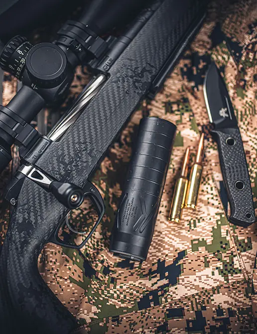 Banish Backcountry suppressor laying next to a rifle and ammo
